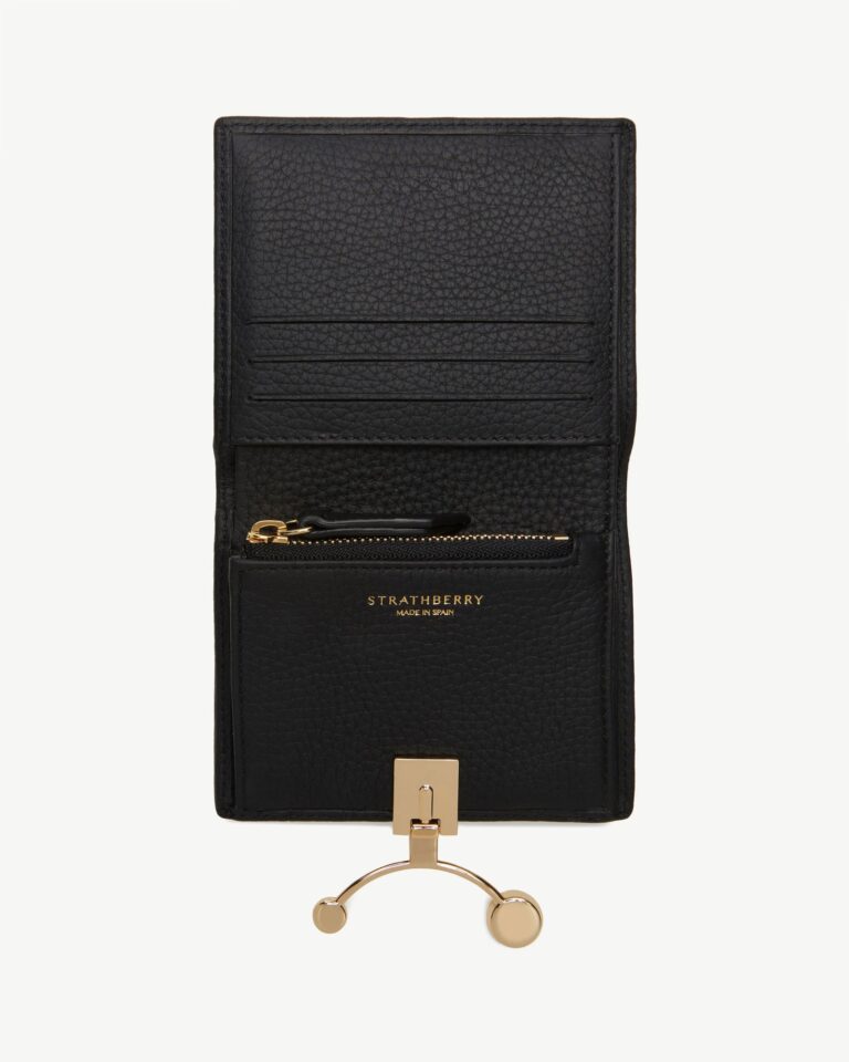 Black leather designer wallet with gold clasp on a neutral editorial background